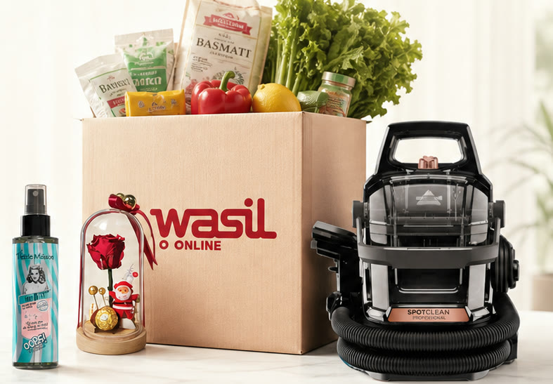 A WasilOnline delivery box packed with fresh groceries, beside a beauty spray, a preserved rose gift dome, and a portable carpet cleaner.